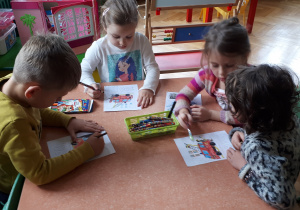 na zdjęciu dzieci z grupy III i V oglądające plakat z numerem alarmowym prezentowany przez nauczyciela